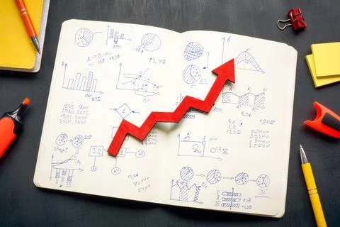 Open notepad with business marks and rising arrow as symbol of success. Stock Photos