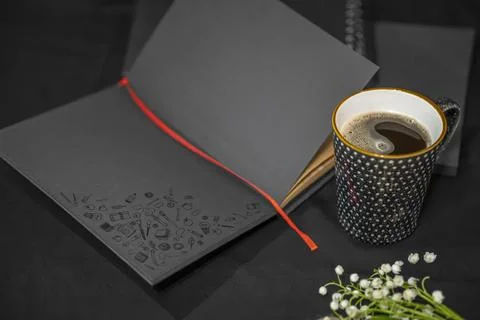 Open notepad, cup of coffee and lilies of the valley on a black background. Foto stock