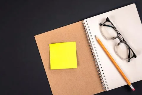 Open notepad, glasses, pencil and blank paper sticker, top view. Foto stock
