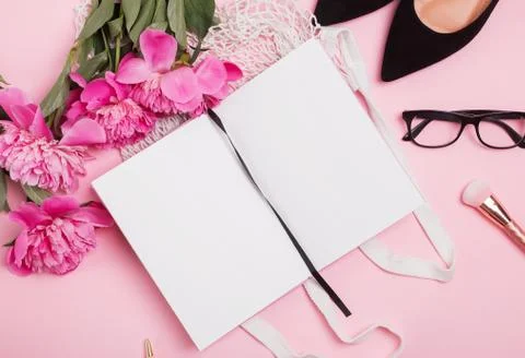Open notepad mock-up on the table with feminine accessories and pink peonies Stock Photos