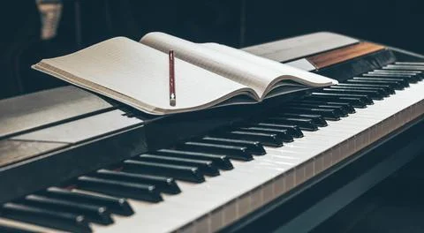 Open notepad on piano keys in the dark, close up. Stock Photos