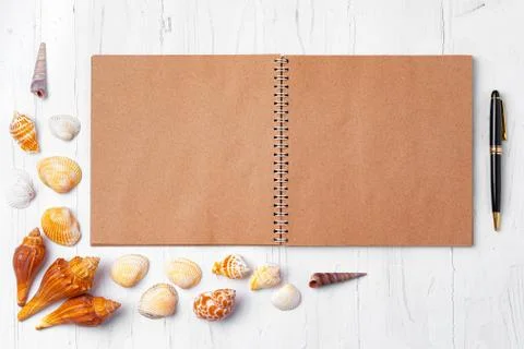 Open notepad with sea shells on white wooden background Stock Photos
