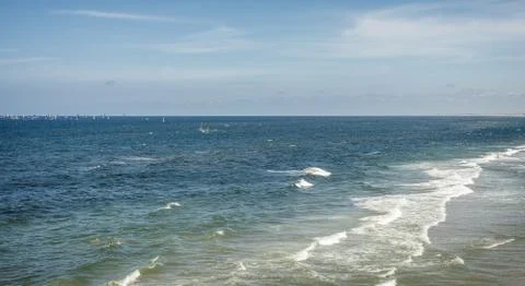 Open ocean with breaking waves on the beach, and sailboats in the distance Stock Photos