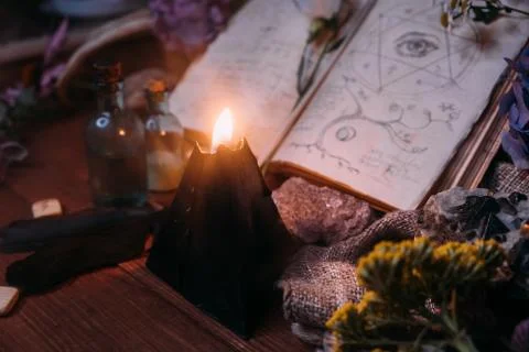 Open old book with magic spells, runes, black candle Foto stock