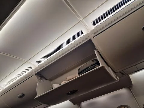 Open overhead compartment with suitcases on the plane Stock Photos