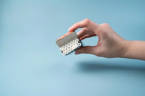 An open pack of cigarettes in a woman's hand on a light blue background. Stock Photos
