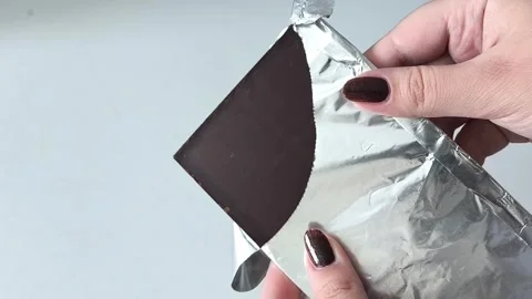 An open pack of dark chocolate. Chocolate bar in foil in a womans hand 库存影片 330156715
