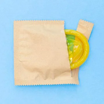 Open pack with yellow condom. Square. Safe or risky sex. Blue background. Stock Photos