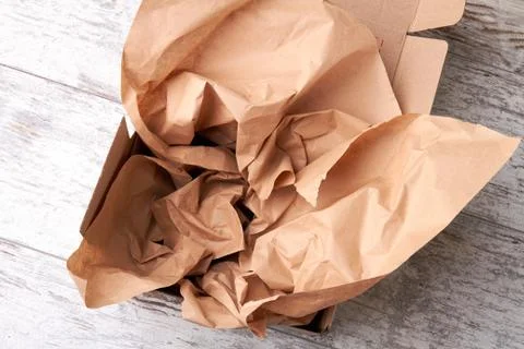 Open packaging box with soft crumpled craft paper inside. Stock Photos