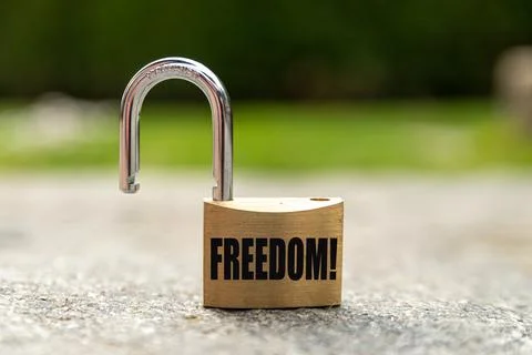 Open padlock placed on a rock floor, with "Freedom" written in black. Stock Photos