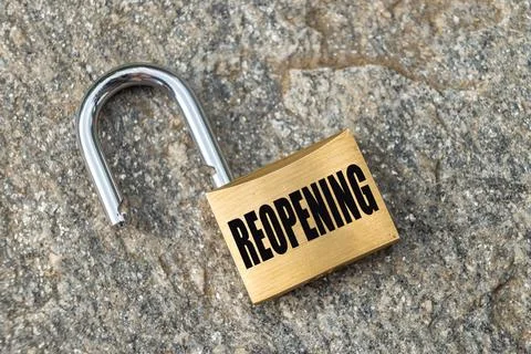 Open padlock placed on a rock surface, with "Reopening" written in black. Stock Photos