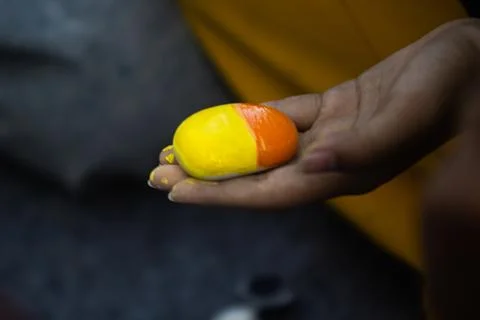 Open Palm Displaying Smooth Round Pebble Half Painted with Yellow and Orang.. Stock Photos