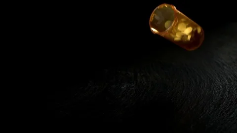 Open pill bottle falling on the black surface in slow motion Stock Footage 81230958