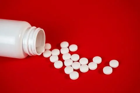 Open pill bottle with scattered white tablets on vibrant red background. Perfect Stock Photos