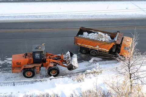 The open pit loader loads snow into a truck after a heavy snowstorm. Stock Photos