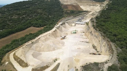 Open-pit quarry with heavy machinery transporting stone in a hillside mining Stock Footage 314337433