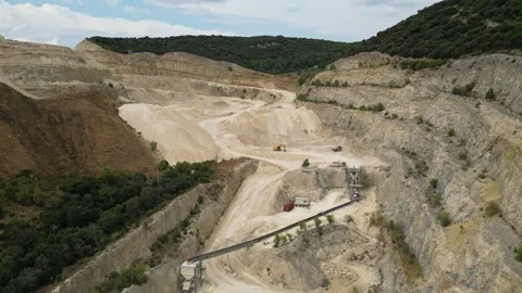Open-pit quarry with heavy machinery transporting stone in a hillside mining Stock Footage 314337756