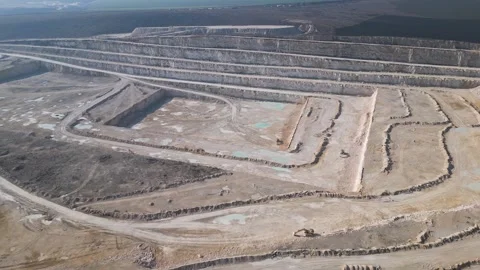 An open-pit quarry with terraced layers and heavy machinery operating on the Stock Footage 300060912