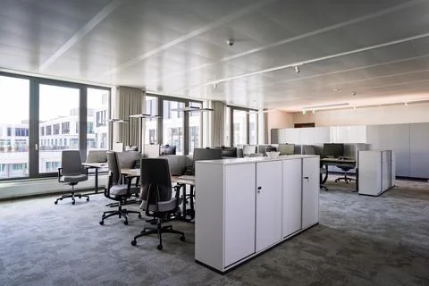 Open-plan office workspace with desks monitors chairs and natural light Stock Photos