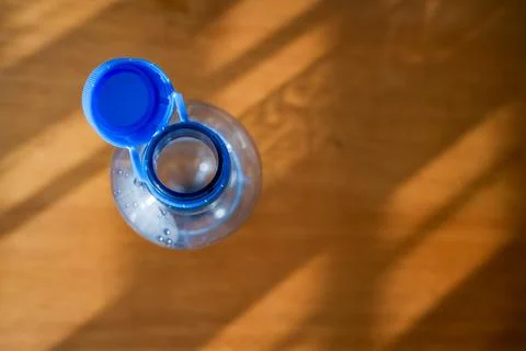 Open plastic bottle with attached blue cap on wooden background in sunlight Stock Photos