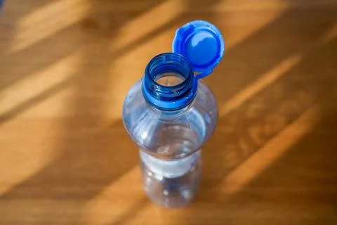 Open plastic bottle with attached blue cap on wooden background in sunlight. Stock Photos