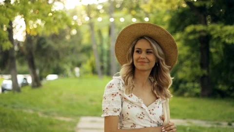 Open portrait of beautiful smiling young woman in straw hat walking in park Stock Footage 242597201