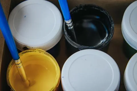 Open pots of blue, black, red, yellow, green and white paint. Stock Photos