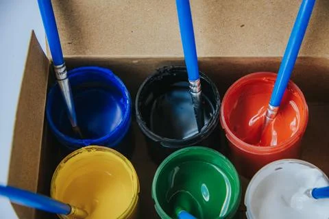 Open pots of blue, black, red, yellow, green and white paint. Stock Photos