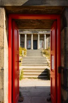 Open red doors frame stone steps leading to classical facade with columns Stock Photos