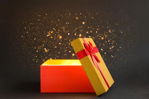 Open red gift box with a bow with a golden glow and glitter inside on a bla.. Stock Photos