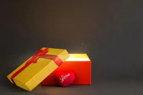 Open red gift box with a bow with a golden glow and glitter inside on a bla.. Stock Photos
