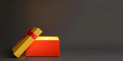 Open red gift box with a bow with a golden glow and glitter inside on a bla.. Stock Photos