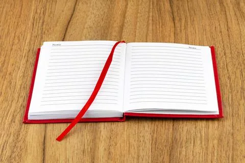 Open red lined notebook lying on a wooden table with a visible ribbon. Stock Photos