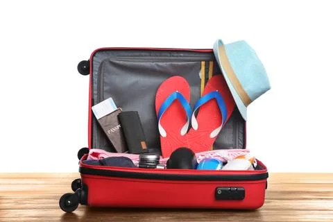 Open red suitcase with different beach objects on wooden table, white backgro Stock Photos