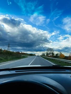 Open road ahead under dramatic blue sky with clouds, viewed from car interior Stock Photos