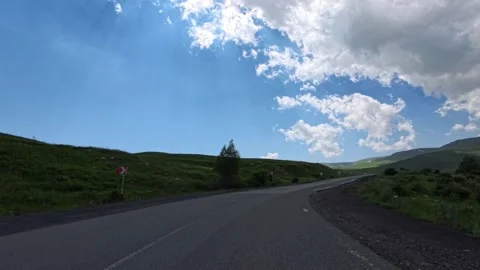 Open road winds through rolling green hills under partly cloudy sky Stock Footage 340078267