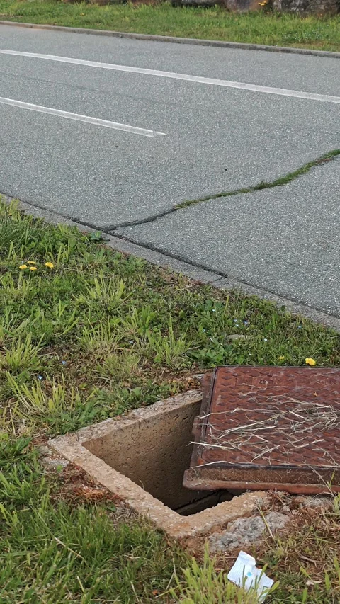 Open rusty manhole cover at road edge on roadside - potential hazard for Stock Footage 332177951