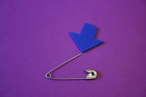 Open safety pin with sharp tip and blue arrow on purple background, danger or ca Fotos Stock