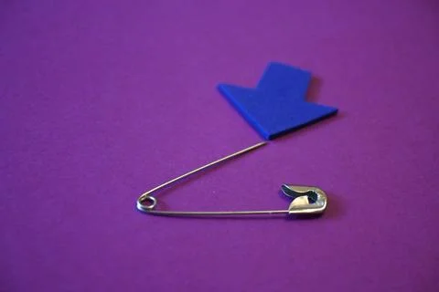 Open safety pin with sharp tip and blue arrow on purple background, danger or ca Photos