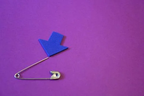 Open safety pin with sharp tip and blue arrow on purple background, danger or ca Stock Photos
