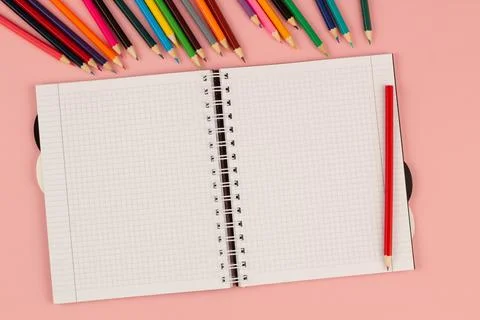 Open school squared notebook and pencils on the pink background. Top view Stock Photos