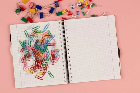 Open school squared notebook and colorful clips on the pink background. Top view Stock Photos