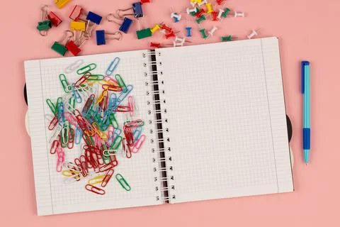 Open school squared notebook and colorful clips on the pink background. Top view Stock Photos