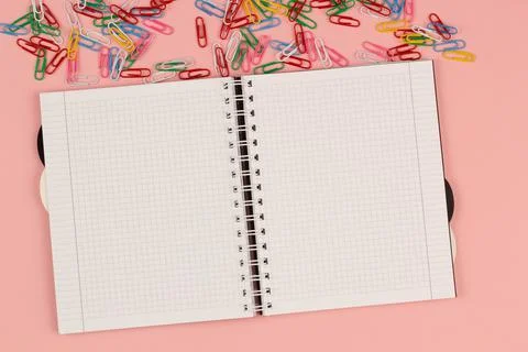 Open school squared notebook and colorful clips on the pink background. Top view Stock Photos