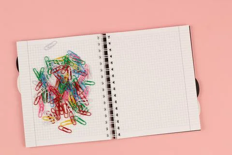 Open school squared notebook and colorful clips on the pink background. Top view Stock Photos