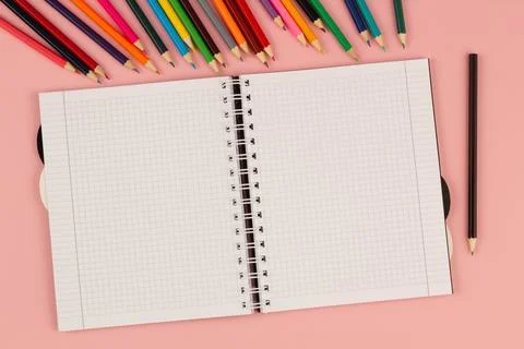 Open school squared notebook and pencils on the pink background. Top view Stock Photos