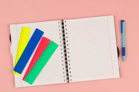 Open school squared notebook and colored rulers on the pink background. Top view Stock Photos