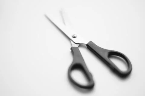 Open scissors with a black handle lie on a white surface 写真素材