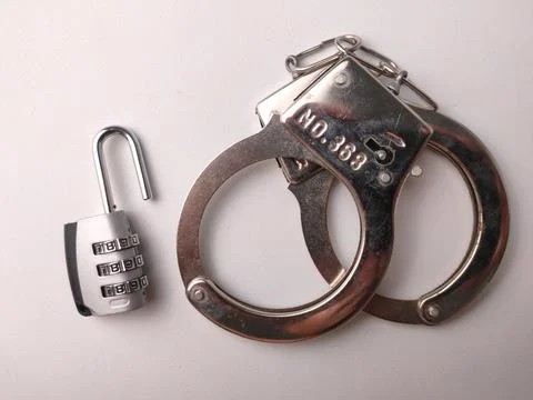 An open silver combination padlock placed next to shiny metal handcuffs on .. Stock Photos