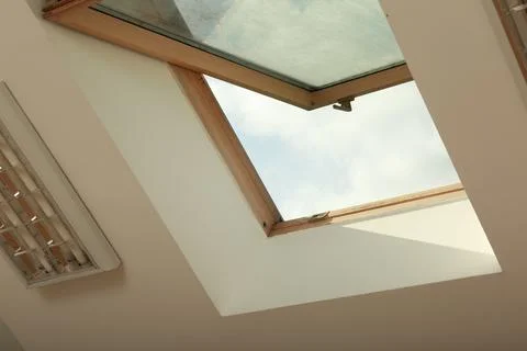 Open skylight roof window on slanted ceiling in attic room, low angle view Stock Photos